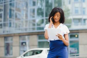 uma bonita africano americano o negócio mulher falando em uma célula telefone às escritório construção foto