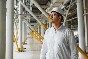 sorridente e feliz funcionário. industrial trabalhador dentro de casa dentro fábrica. jovem técnico com branco Difícil chapéu. foto