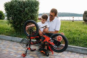 feliz pai e dele filho tendo Diversão juntos às a verde parque, fixação bicicleta junto. do pai dia. foto