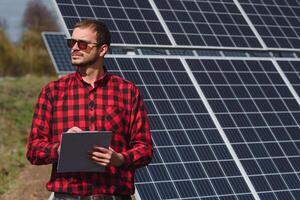 retrato do homem com uma tábua dentro dele mãos em pé perto a solar painéis estação. verde ecológico poder energia geração. solar estação desenvolvimento conceito. casa construção. foto