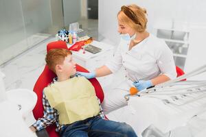 dentista vestindo mascarar. ruivo criança dentista vestindo mascarar examinando fofa Garoto foto