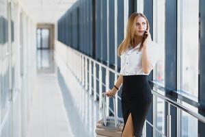 retrato do jovem atraente empresária falando em Smartphone com dela mala de viagem dentro aeroporto foto