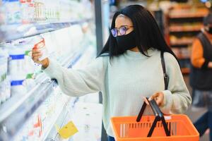 africano mulher vestindo descartável médico mascarar. compras dentro supermercado durante coronavírus pandemia surto. epidemia Tempo foto