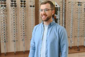 assistência médica, visão e visão conceito. feliz homem escolhendo óculos às óptica loja, seletivo foco foto