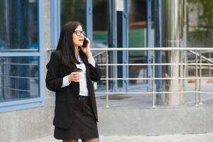 advogado empresária profissional caminhando ao ar livre falando em célula inteligente telefone bebendo café a partir de descartável papel copo. foto