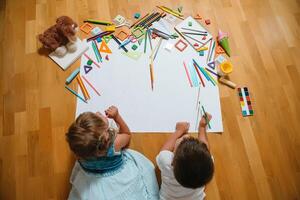 crianças desenhando em chão em papel. pré escola Garoto e menina jogar em chão com educacional brinquedos - blocos, trem, Ferrovia, avião. brinquedos para pré escola e Jardim da infância. crianças às casa ou creche. topo visualizar. foto