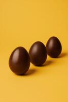 ai gerado três isolado chocolate ovos em uma uma vibrante amarelo fundo, apresentando uma negrito e minimalista Páscoa celebração. moderno marketing campanhas ou negrito gráfico desenhos foto