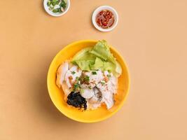 tailandês Comida fatiado peixe mingau dentro uma tigela com sopa, Pimenta molho e Primavera cebola topo Visão em de madeira mesa foto