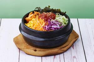 coreano Comida arroz bibimbap com vegetais, carne e teriyaki dentro uma Preto tigela em madeira tabela fundo foto