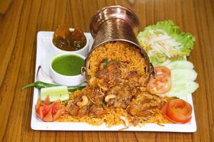 frango Biryani com salada, raita, hortelã molho picante e salmoura servido dentro uma balde isolado em Sombrio fundo lado Visão do indiano picante Comida foto