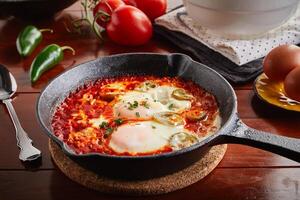 Shakshuka servido dentro uma fritar panela isolado em de madeira fundo lado Visão do árabe Comida foto