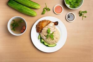 cozido no vapor e assado frango arroz com cru pepino, coentro, salada, molho e sopa servido dentro uma prato isolado em de madeira fundo topo Visão foto