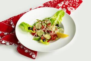 fresco saudável verde salada dentro uma prato isolado em colorida mesa pano topo Visão em cinzento fundo tomate, pepino, cebola, espinafre, alface e sésamo foto