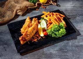 frito vermelho tilápia peixe com salada, Lima e fritas dentro uma prato lado Visão em Sombrio fundo foto
