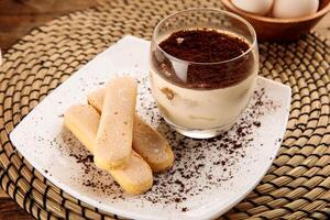 Tiramisu com dedo biscoitos servido dentro uma vidro isolado em de madeira fundo lado Visão sobremesa foto