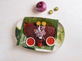 tradicional churrasco arraia servido em banana folha com cebolas, vermelho Pimenta chili molho e limão em uma branco prato topo Visão foto