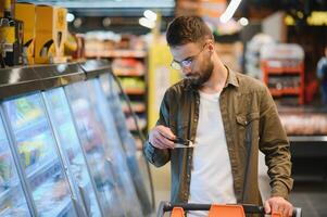 uma bonito jovem homem dentro uma mercearia loja escolhe Comida produtos. foto