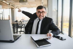 Bravo homem de negocios sentado às a mesa e gritando sobre. foto