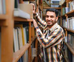 feliz inteligente indiano ou árabe cara, misturado raça macho, universidade estudante, dentro a biblioteca foto