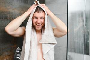 homem com molhado cabelo aguarde toalha depois de banho. manhã lavando, despertar acima, todo dia vida. refresco, assistência médica. higiene, sexy cara lavar, spa, relaxar. homem dentro banheiro com muscular corpo em cinzento fundo foto