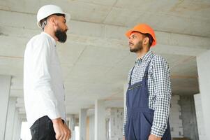 multirracial masculino colegas de trabalho dentro capacetes discutindo projeto em construção local foto