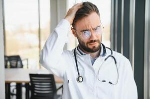 estressado masculino doutor. meio adulto masculino médico trabalhando grandes horas. sobrecarregado médico dentro dele escritório. não até médicos estão isentar a partir de esgotamento foto