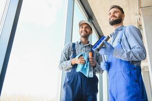 multiétnico profissional limpadores dentro uniforme lavando ampla janelas dentro escritório foto