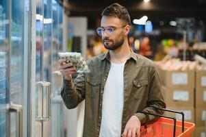 retrato do sorridente bonito homem mercearia compras dentro supermercado, escolhendo Comida produtos a partir de estante foto