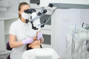 fêmea dentista usando dental microscópio tratando paciente dentes às dental clínica escritório foto