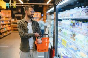 retrato do sorridente bonito homem mercearia compras dentro supermercado, escolhendo Comida produtos a partir de estante foto