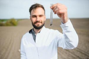 laboratório trabalhador segurando profissional artigos de vidro e teste Preto solo depois de colheita dentro a campo foto