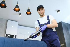 limpeza serviço. homem zelador dentro luvas e uniforme vácuo limpar \ limpo sofá com profissional equipamento. foto