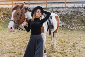 feliz elegante jovem mulher posando com uma cavalo em a de praia foto