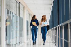 dois jovem mulheres com livro conversando enquanto em pé dentro Faculdade corredor. universidade alunos dentro corredor depois de a palestra. foto