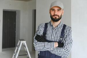 retrato do bonito mecânico com restolho dentro azul geral, camisa tendo dele braços cruzado, olhando às Câmera foto