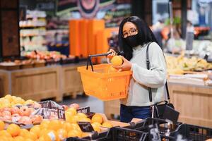 africano mulher vestindo descartável médico mascarar. compras dentro supermercado durante coronavírus pandemia surto. epidemia Tempo foto