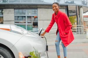 africano americano menina cobrando eletro carro às a elétrico gás estação foto