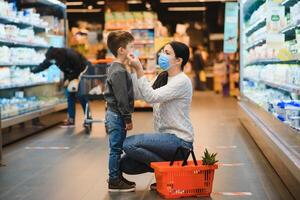 compras com criança durante vírus surto. mãe e criança vestindo cirúrgico face mascarar comprando fruta dentro supermercado. mãe e pequeno Garoto Comprar fresco vegetal dentro mercearia loja. família dentro fazer compras foto