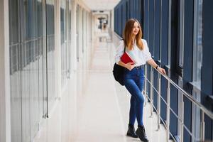 retrato do uma bonita fêmea aluna com livros e uma mochila dentro a universidade corredor foto