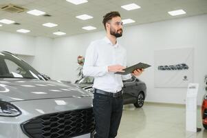 fechar-se tiro do bem sucedido confiante sorridente caucasiano masculino fazer compras assistente segurando prancheta dentro formal roupas às automóvel carro revendedor fazer compras foto