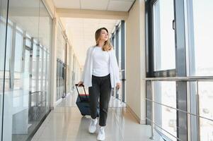 jovem bonita à moda mulher com bagagem às a internacional aeroporto. esperando dela voar às imposto livre compras zona. foto