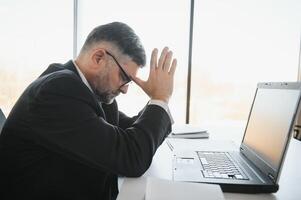 cansado estressado escritório trabalhador sentado às escrivaninha e pensamento, ele é fricção dele olhos e sentindo-me Exausta. foto