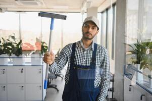 jovem indiano homem lavando janela dentro escritório. foto