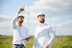 uma equipe do masculino engenheiros trabalhando juntos às vento turbina gerador Fazenda. foto