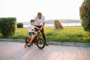 jovem e feliz pai ensina dele jovem filho para passeio uma bicicleta. a criança é feliz . pai assistindo filho. do pai dia foto