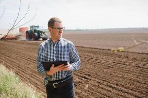 jovem agricultor em terras agrícolas com trator dentro fundo foto