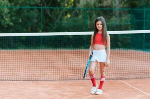 criança jogando tênis em ao ar livre tribunal. pequeno menina com tênis raquete e bola dentro esporte clube. ativo exercício para crianças. verão Atividades para crianças. Treinamento para jovem miúdo. criança Aprendendo para jogar foto