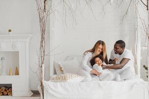 animado multirracial jovem família com pequeno menina criança ter diversão, muito feliz feliz. internacional mãe e Papai jogar com pequeno garota, apreciar final de semana às casa juntos foto