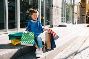 retrato do lindo sorridente pequeno menina vestindo com compras saco ao ar livre foto