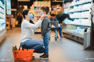mãe e dela filho vestindo protetora face mascarar fazer compras às uma supermercado durante a coronavírus epidemia. foto